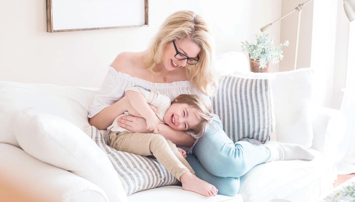 A mother laughing with her young son on the couch at home